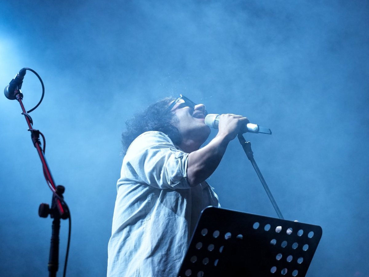 Un chanteur au micro sur scène, dans la fumée et la lumière bleue